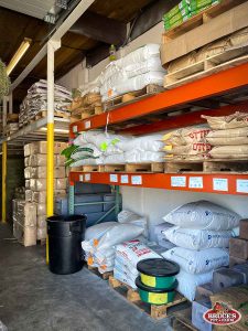 Bruce's Pet and Farm Supply warehouse section with shelves stocked with various types of livestock feed, soil amendments, and farm supplies. Large bags of feed, minerals, and bedding materials are organized on pallets, catering to the needs of farmers and livestock owners. The well-organized storage area provides easy access to essential products for animal nutrition and farm maintenance in the Maple Ridge community.