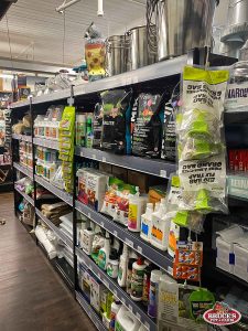 Bruce's Pet and Farm Supply shelves filled with a variety of gardening and pest control products, including plant fertilizers, insect repellents, soil enhancers, and decorative garden items like metal buckets and an owl statue. The store provides a comprehensive selection of supplies for gardeners and homeowners looking for quality products to support healthy plants and manage pests.